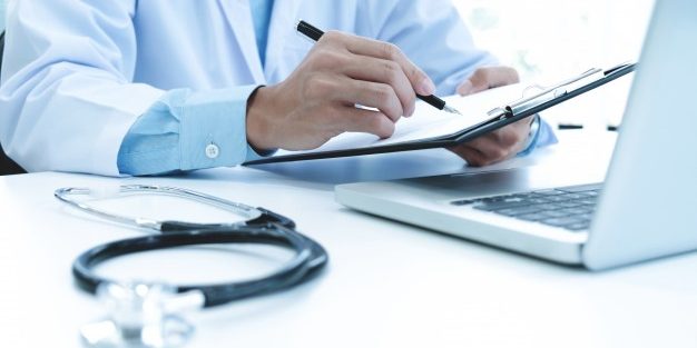 doctor-working-with-laptop-computer-writing-paperwork-hospital-background_1421-69